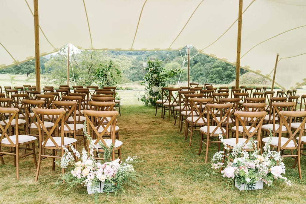 set up of wedding chairs in a marquee outside with flowers at entrance